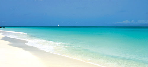 Scene of a blue sky, turquoise ocean, white beach and a distant sail boat. Scene of a blue sky, turquoise ocean, white beach and a distant sail boat.